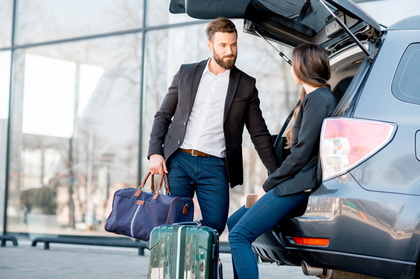 Business travelers preparing for an airport transfer, with a man holding a stylish duffel bag and a woman sitting on the back of an SUV with their luggage. Convenient and professional airport transfer services ensure a smooth journey for corporate clients