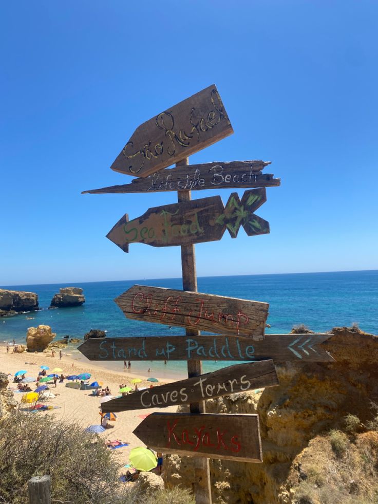 Wooden signpost with directions on a beach with rocky cliffs.